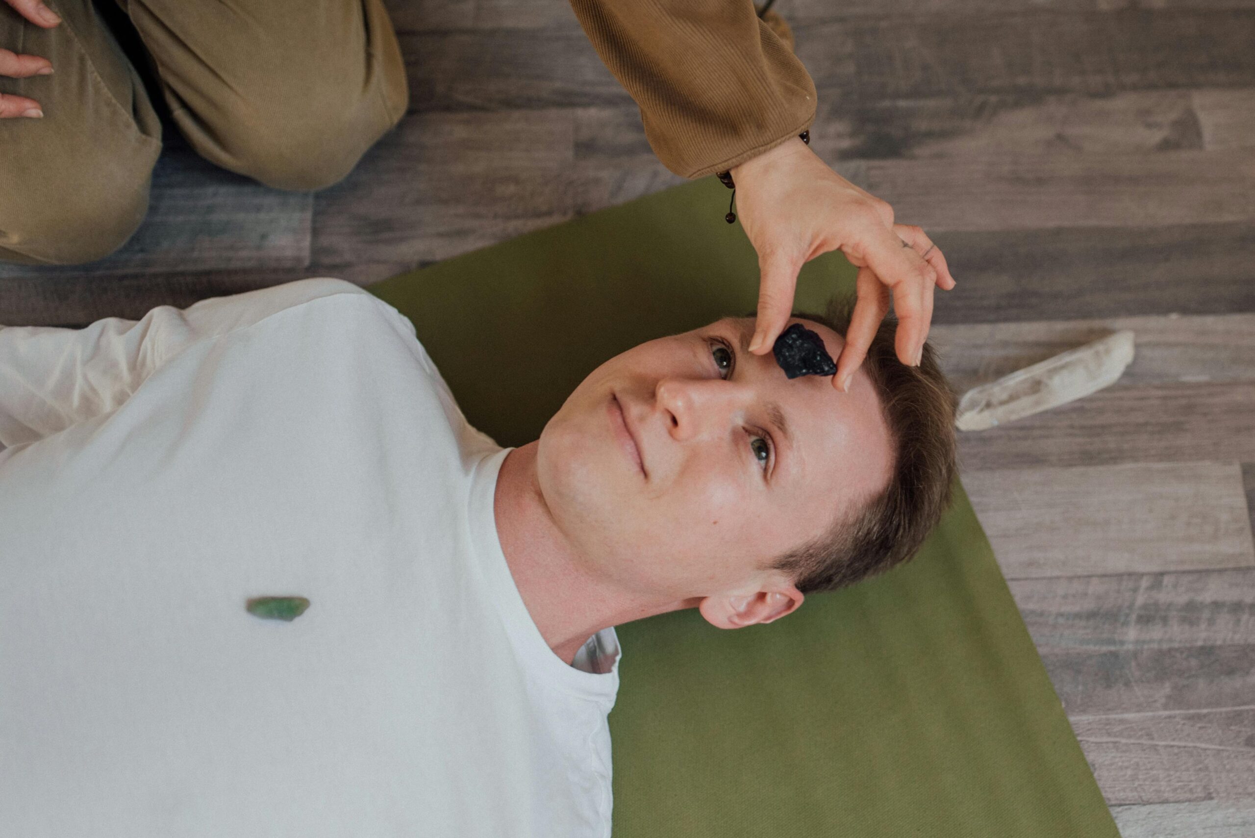 A man lying down during a crystal healing ritual indoors on a yoga mat.