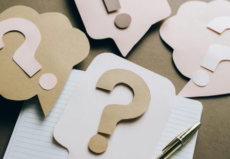 Artistic paper question marks on an open notebook with a pen, symbolizing curiosity and creativity.